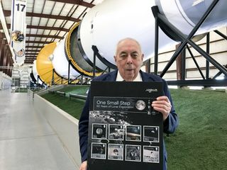 George Abbey poses with postage stamps for the 50th anniversary of Apollo inside the Saturn V building at Johnson Space Center's rocket park in 2019.