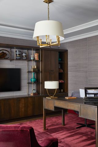 Home office with dark wood bespoke cabinetry and shelving, dark wood desk, pendant and desk light and deep red rug
