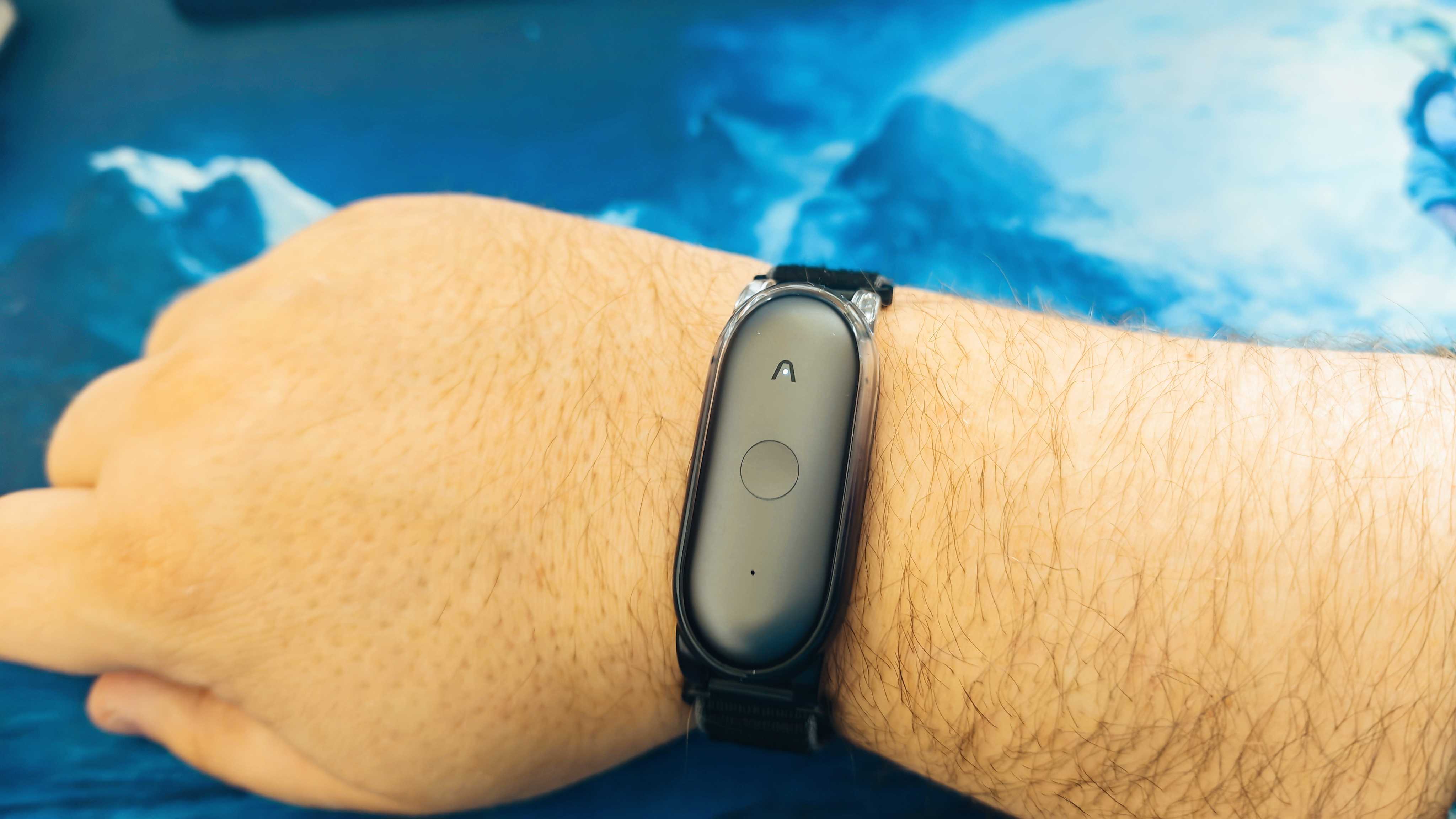 A wearable Plaud NotePin S AI voice recorder on a blue desk surface