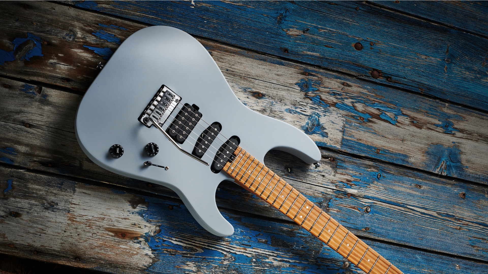 A Charvel Pro-Mod DK24 HSS electric guitar lying on a worn, blue wooden floor