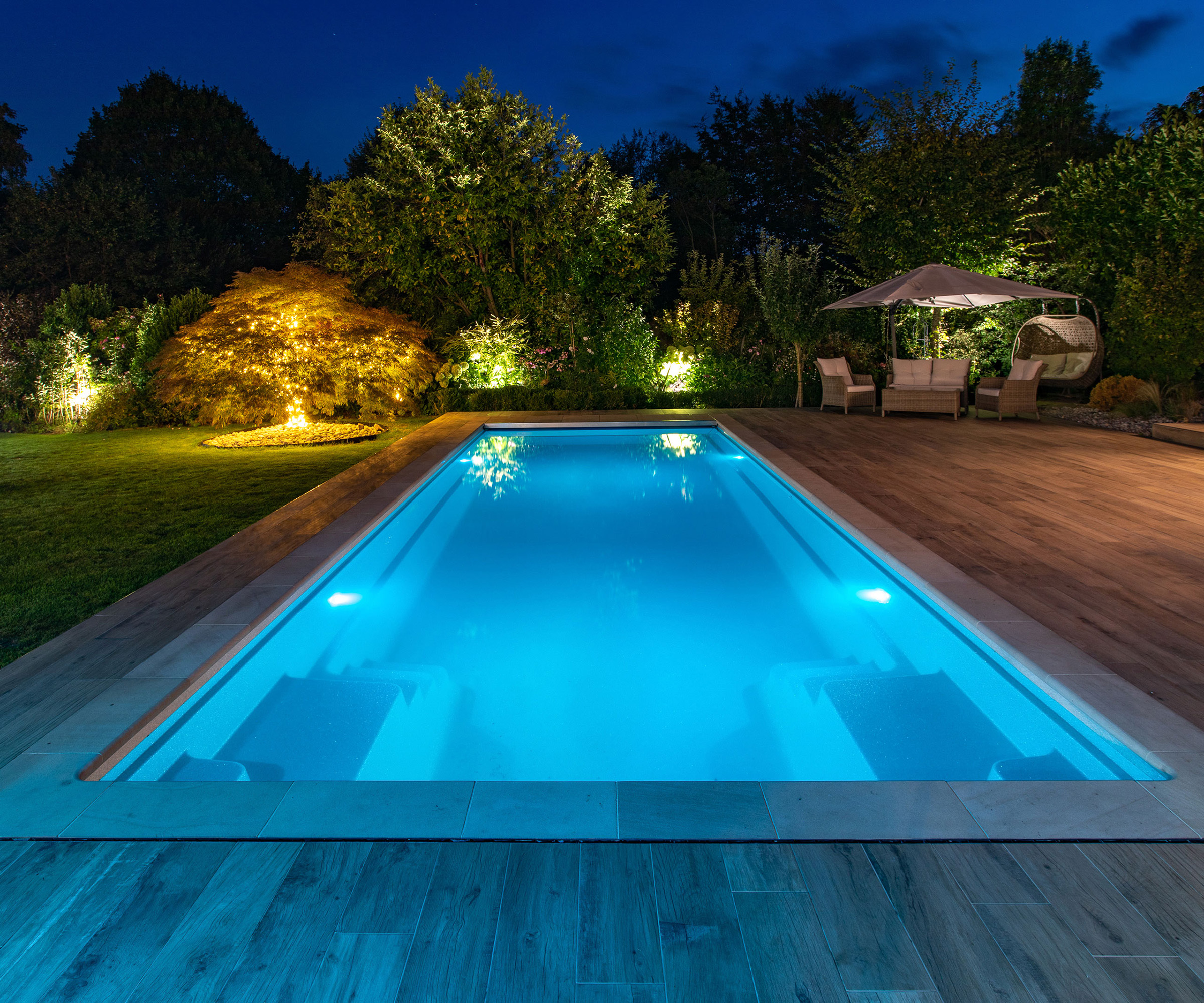 A rectangular pool lit up at night in a garden scheme