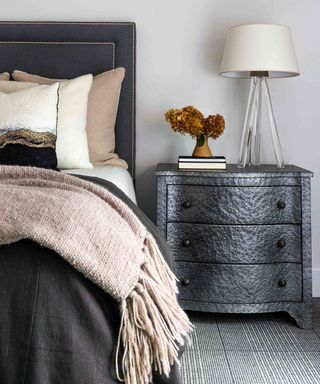 Small bedroom space with bed and dark gray bedside table accented with ochre dried hydrangeas
