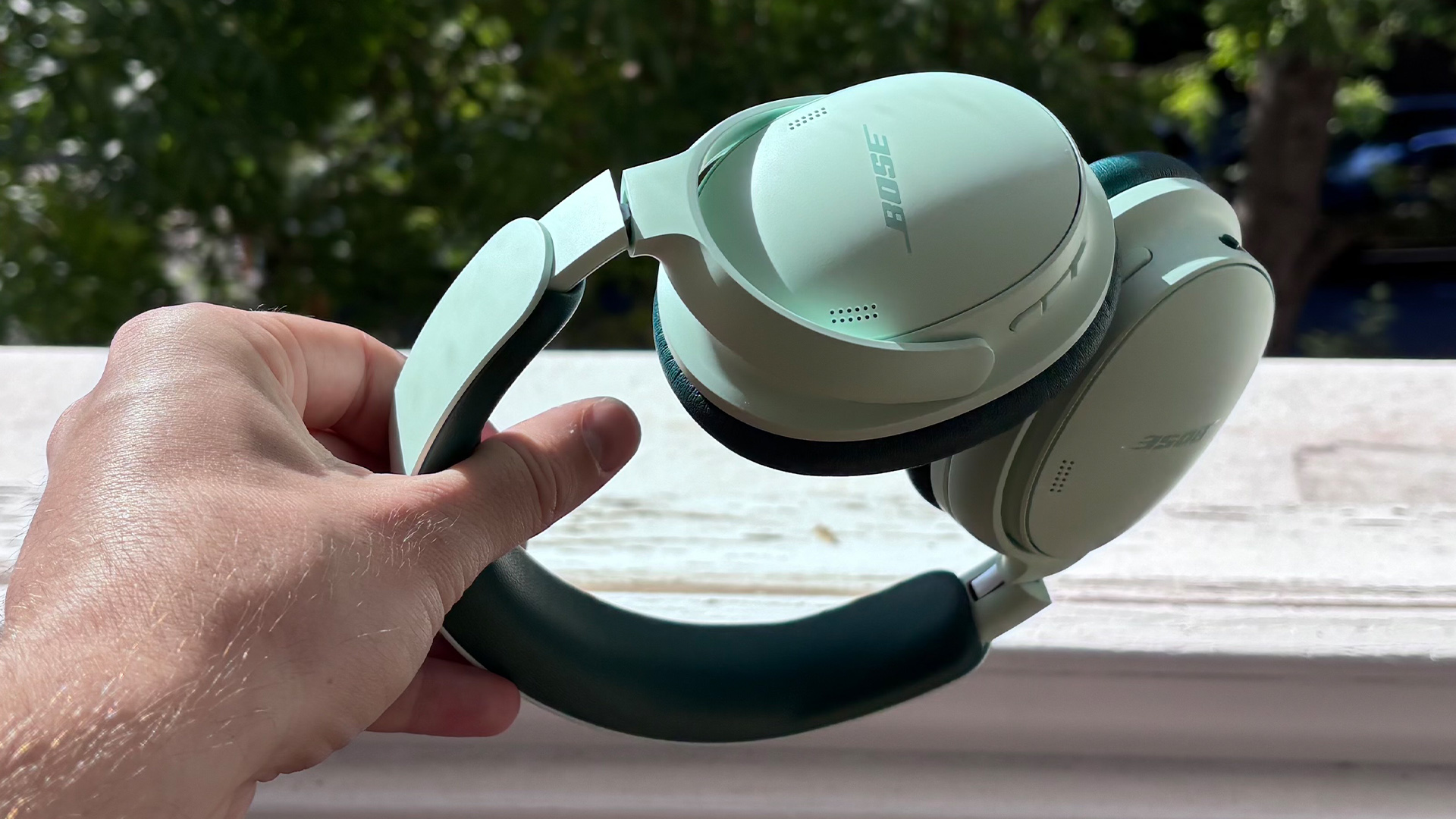 Bose QuietComfort Headphones (2nd Gen) over-ear headphones held in hand outdoors in sunshine