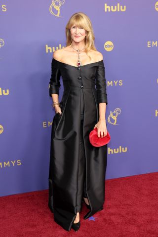 Laura Dern wears an off-the-shoulder black gown with pockets and a long necklace.