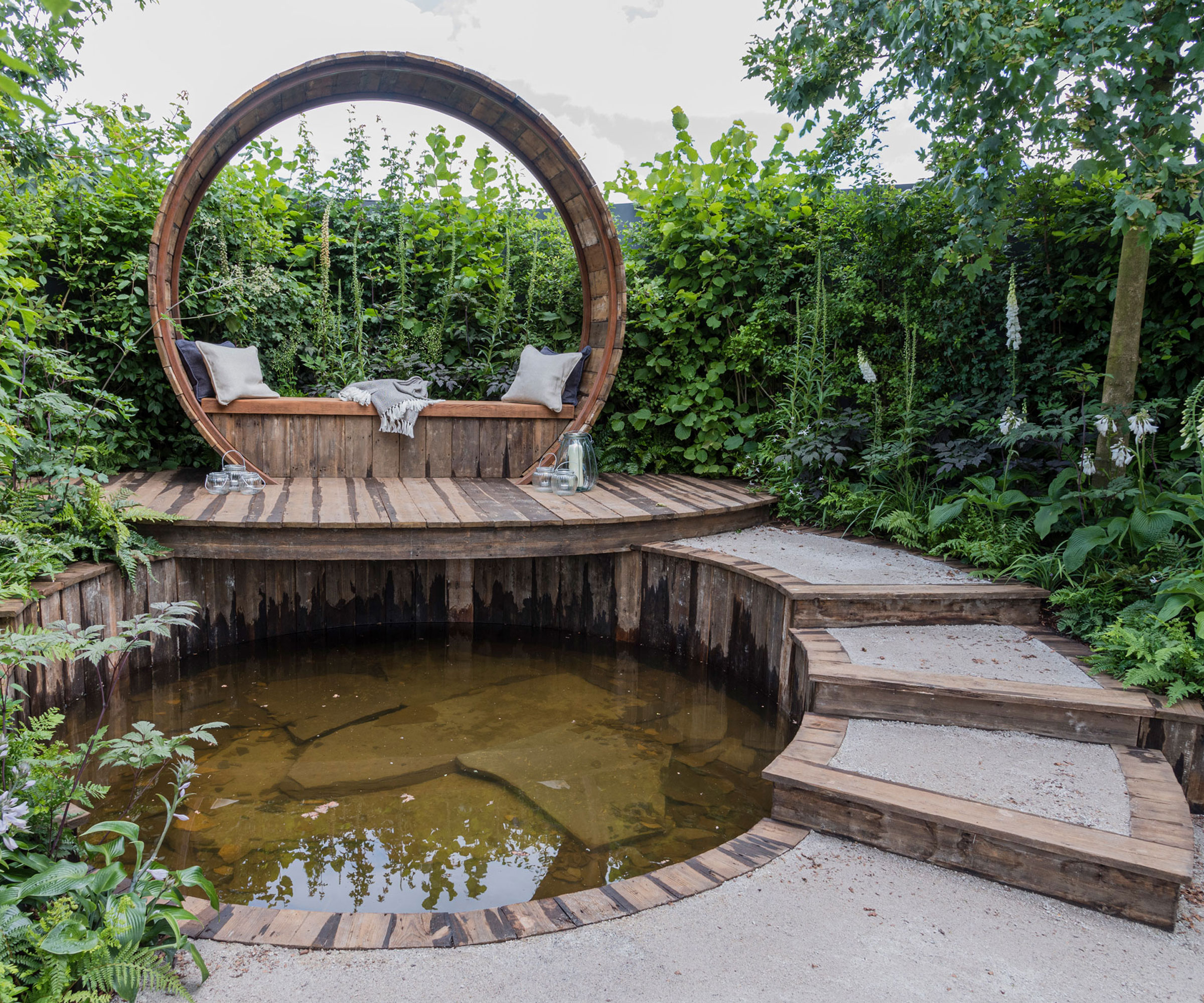 pond design with elevated deck and seating area, and path leading to it, surrounded by shrubs, trees and flowers