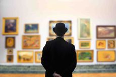 silhouette of a man looking at framed art on a wall