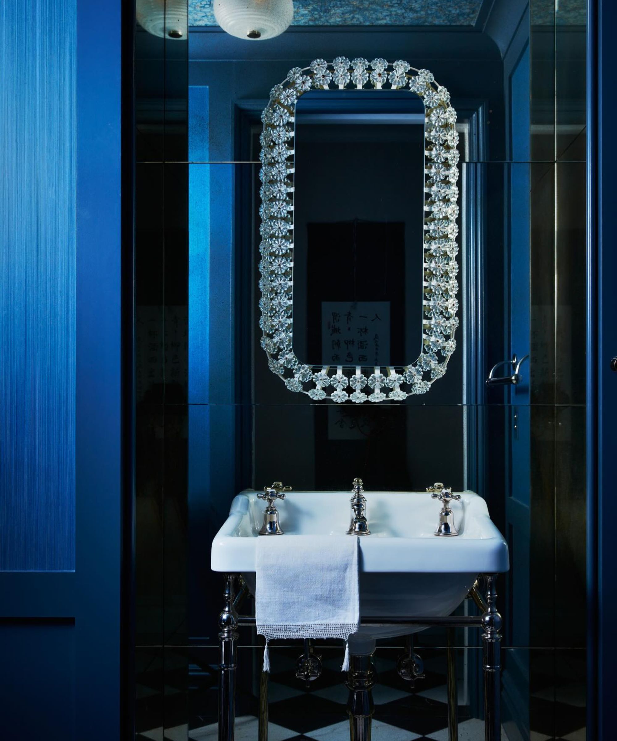 A powder room with cobalt blue walls, a blue wallpapered ceiling, a white sink, and a decorative mirror.