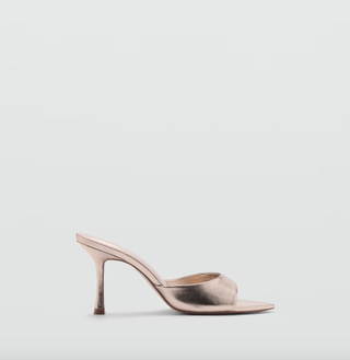 a pair of metallic mule sandals in front of a plain backdrop