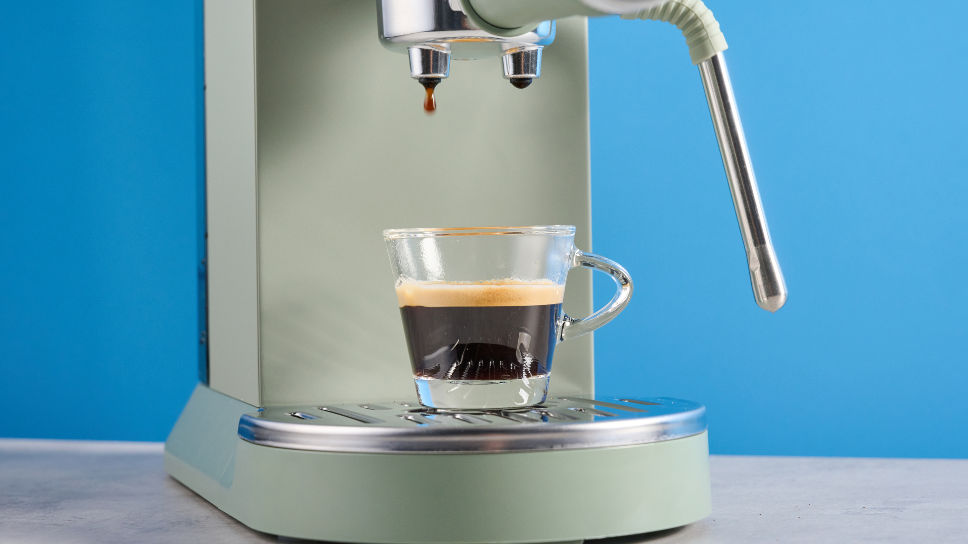 DeLonghi Dedica Duo in the green colorway with accessories photographed on a blue background.