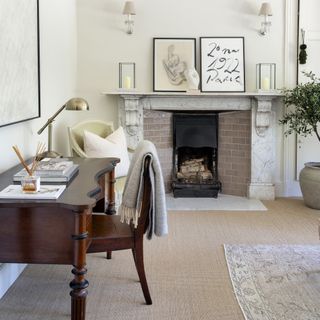 living room with beige carpets, wooden desk and chair, cream walls, fireplace and marble mantel