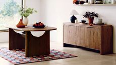 Image of a blue and red modern geometric rug under a wooden dining table in a white room with concrete floors. 