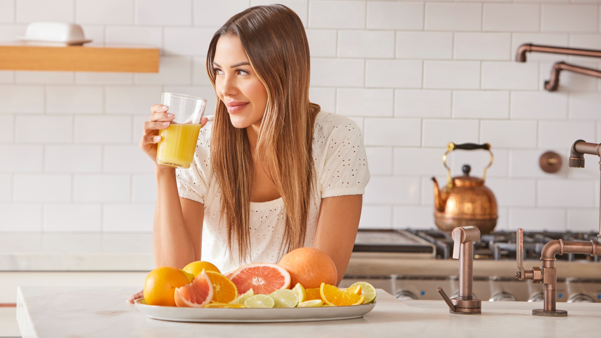 Woman drinking grapefruit juice drink in kitchen with a plate of grapefruit in front of her