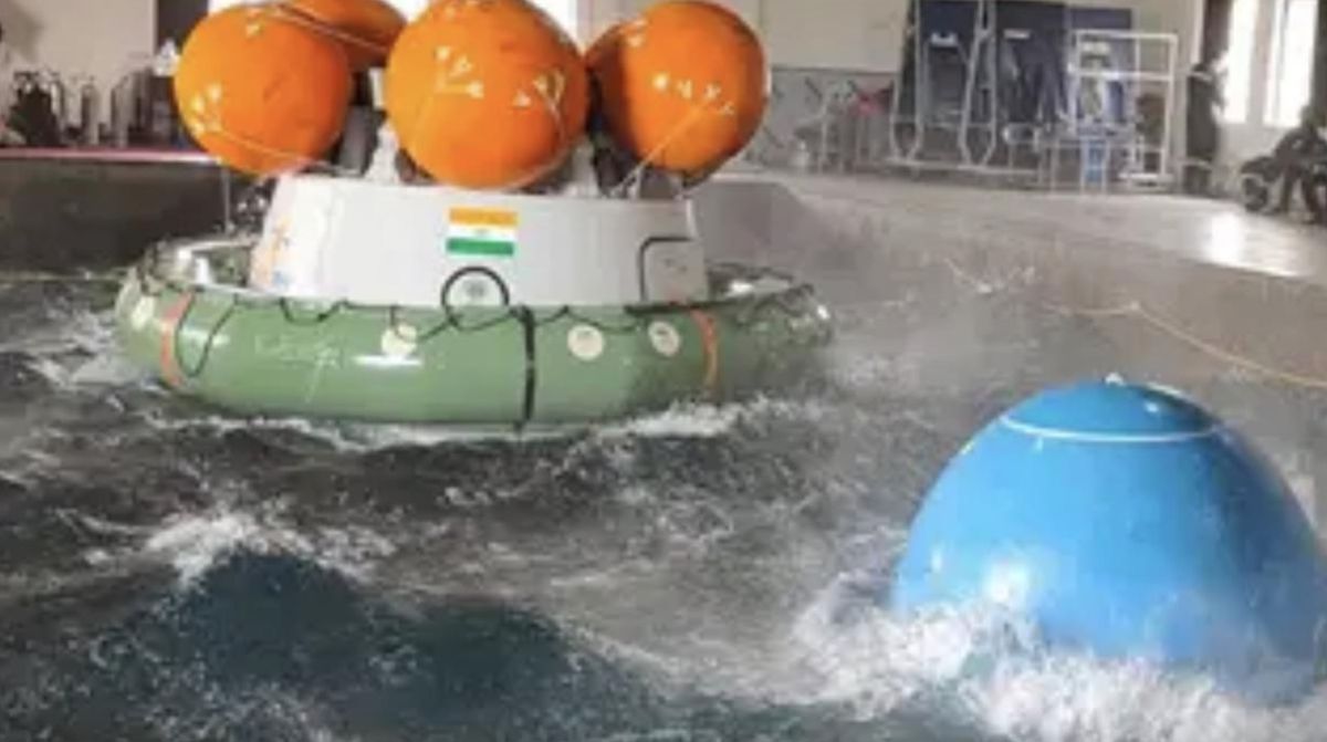 a crew capsule with inflated orange ball-shaped floats rests in an indoor pool during a test.