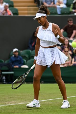 Naomi Osaka of Japan reacts against Diane Parry of France in the Ladie's Singles first round match during day one of The Championships Wimbledon 2024 at All England Lawn Tennis and Croquet Club on July 01, 2024 in London, England. She's wearing a white ruffled Nike tennis top, visor, and sheer paneled miniskirt.