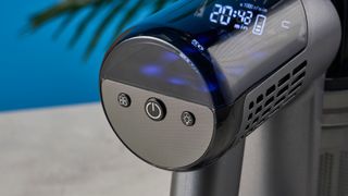 a closeup shot of the buttons on a modern-looking sleek shiny vacuum cleaner with light grey components on a carpet in front of a blue background