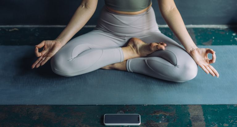 Best meditation apps, an unrecognizable woman meditating in lotus position with her mobile phone on the floor in front of her