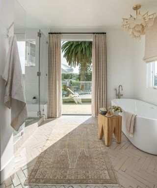 Neutral, calming bathroom with bathtub, rug, shower and open-doors looking out to the garden