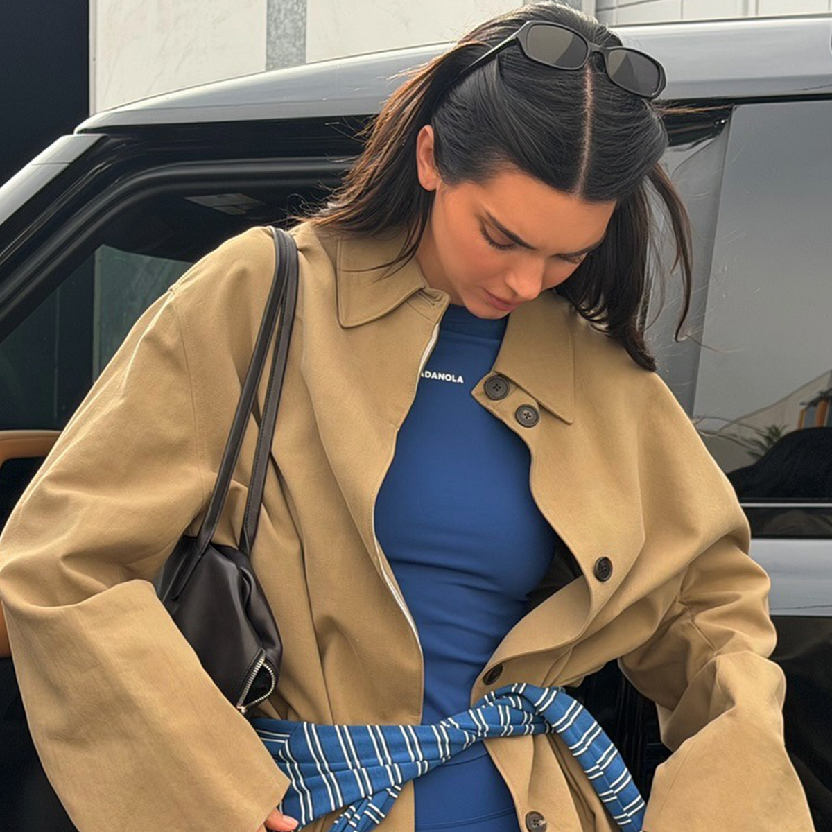 Kendall wears a beige car coat, blue top, and blue stripe shirt wrapped around her waist.