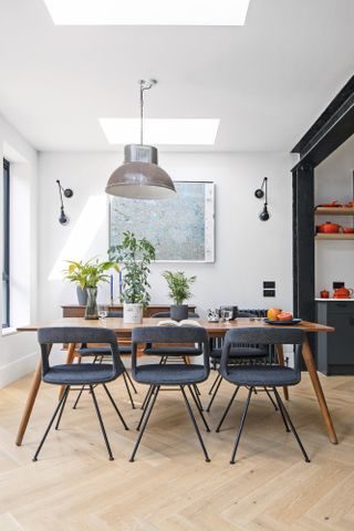 Dining area under rooflights with oak chevron flooring, wood mid-century table, charcoal mid-century chairs and large statement pendant light above