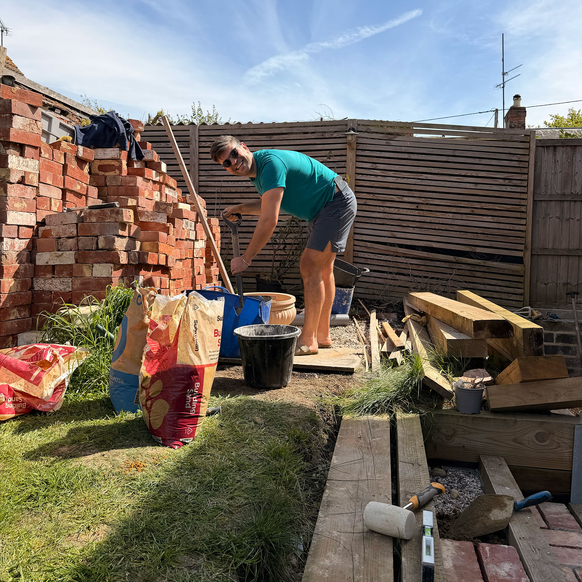 Man in garden by wooden fence and large pile of bricks