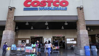The Costco Wholesale Corporation website is displayed on a laptop in the background with a hand holding a bank card.