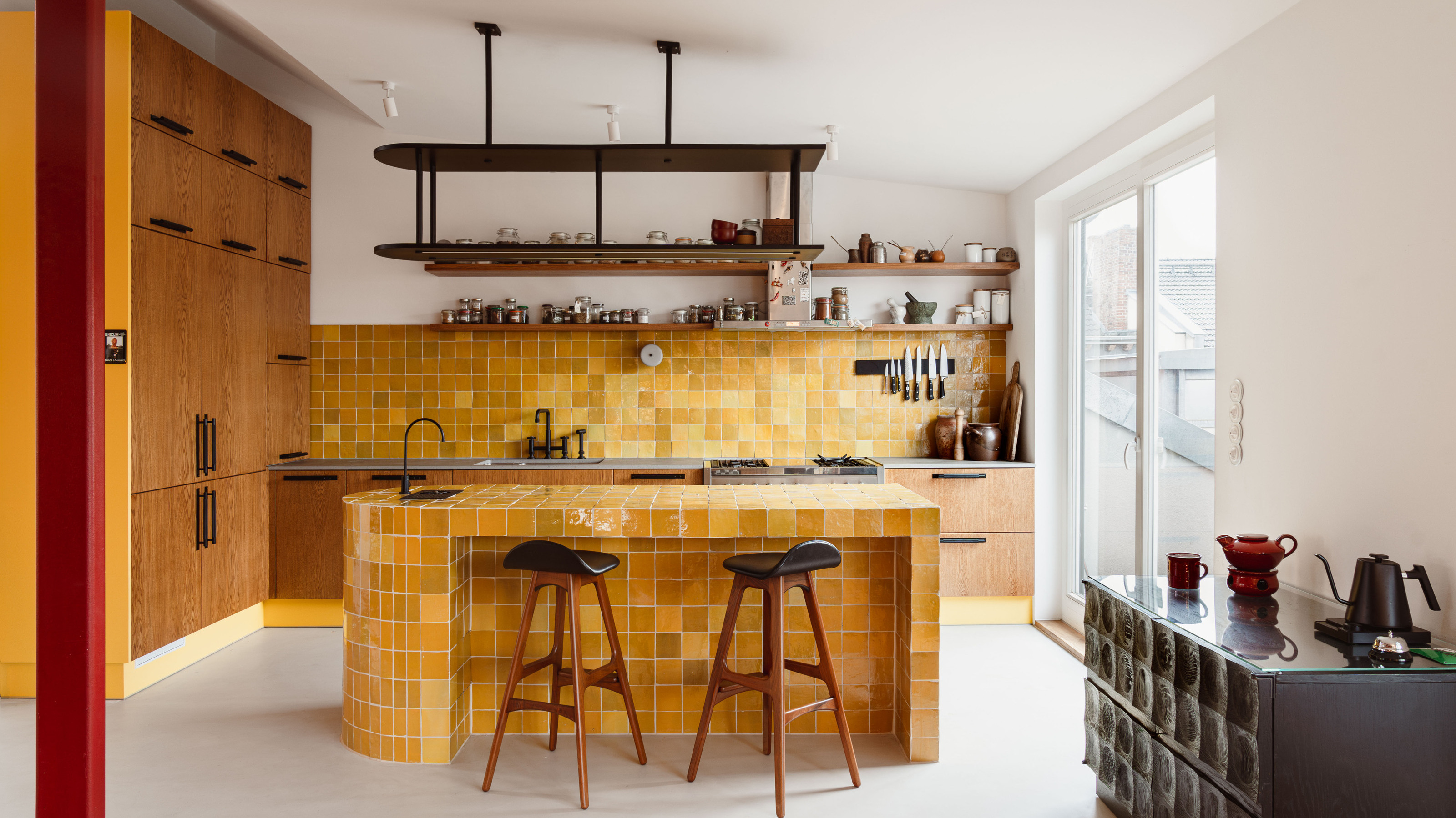 A kitchen with wooden wall cabinetry on one end, a yellow zellige tile backsplash, and a matching curved island
