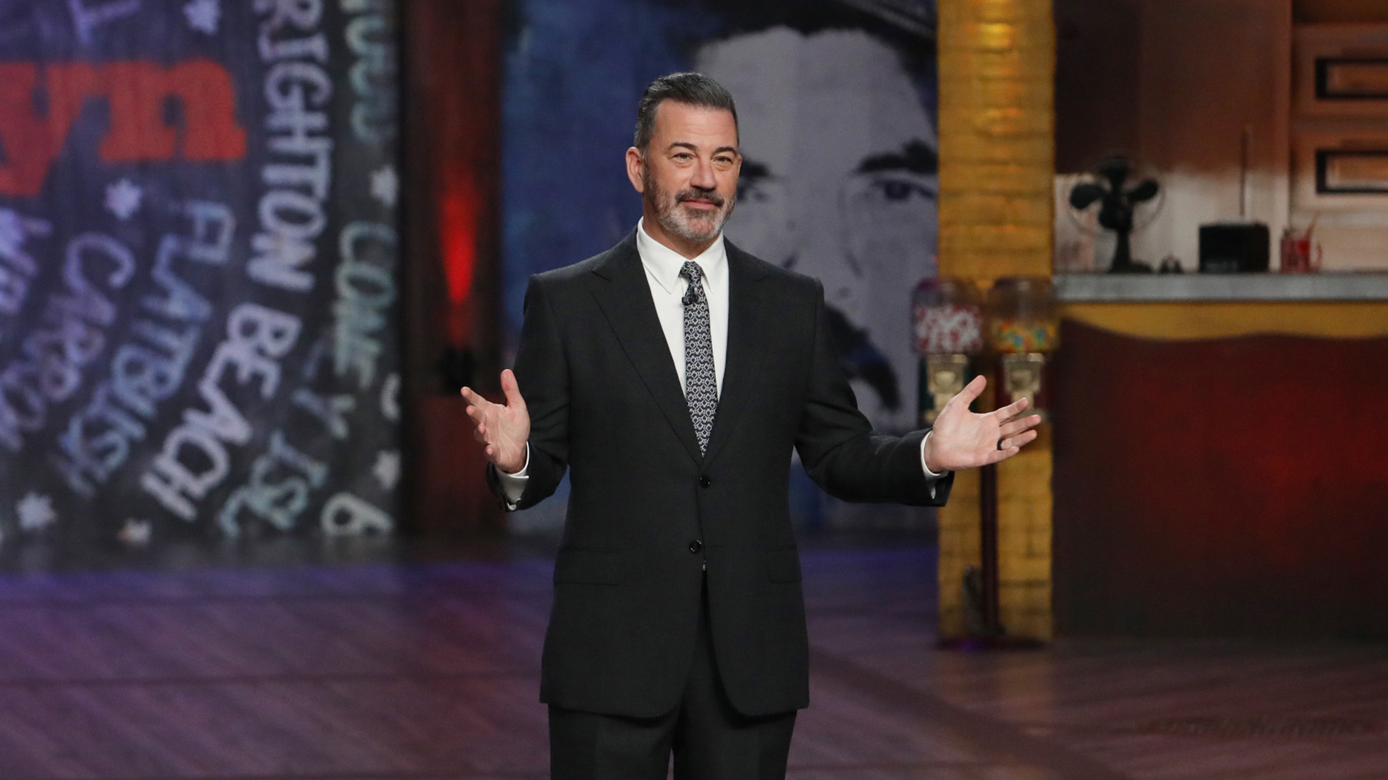 Jimmy Kimmel holds his hands up during his monologue in Brooklyn October 2026. He is wearing a black suit and grey tie.