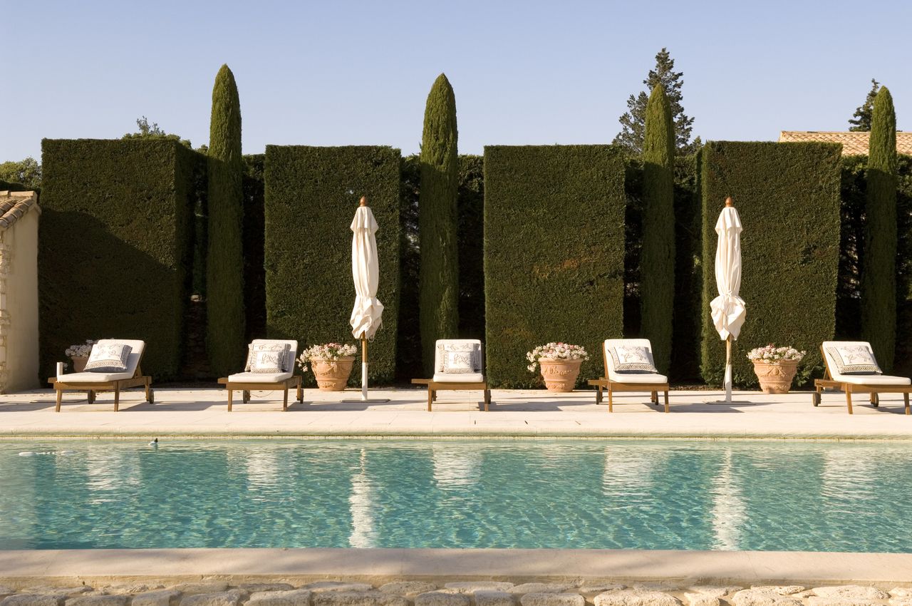 Luxury pool with lounge chairs and hedges.