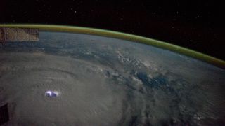 A photo of Earth from orbit showing a lightning strike in a cyclone and the curvature of the Earth surrounded by golden airglow