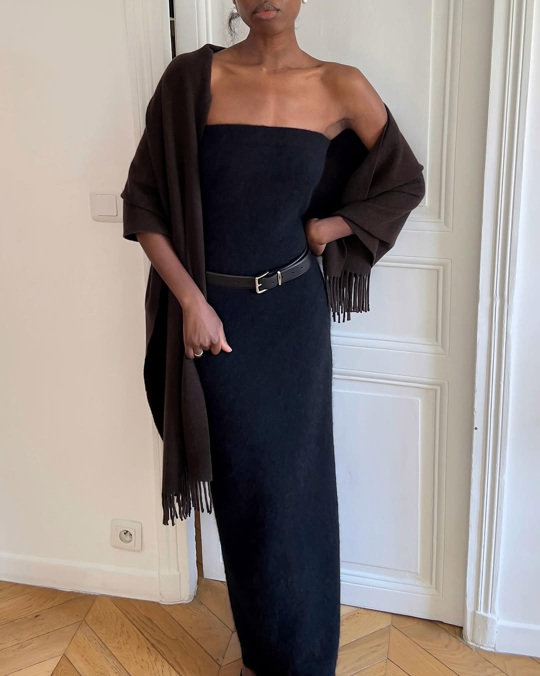 Woman wearing a black maxi dress and fringed shawl.