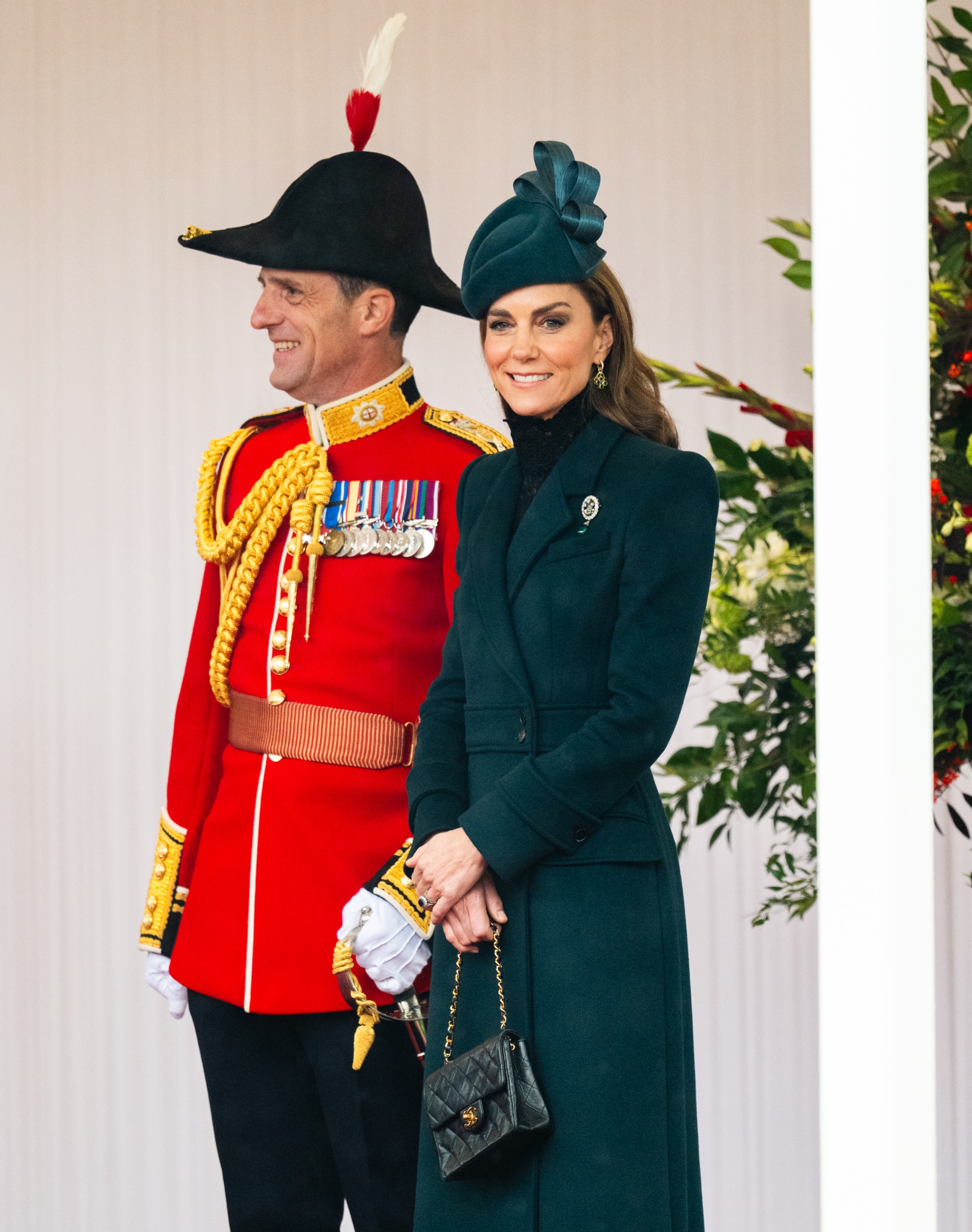 Princess Kate wearing a green coat and hat, posing with a man in a red military uniform