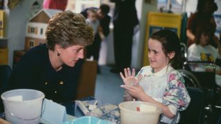 Princess Diana in a black suit sat talking to a child whos a patient at the Great Ormand Street Hospital