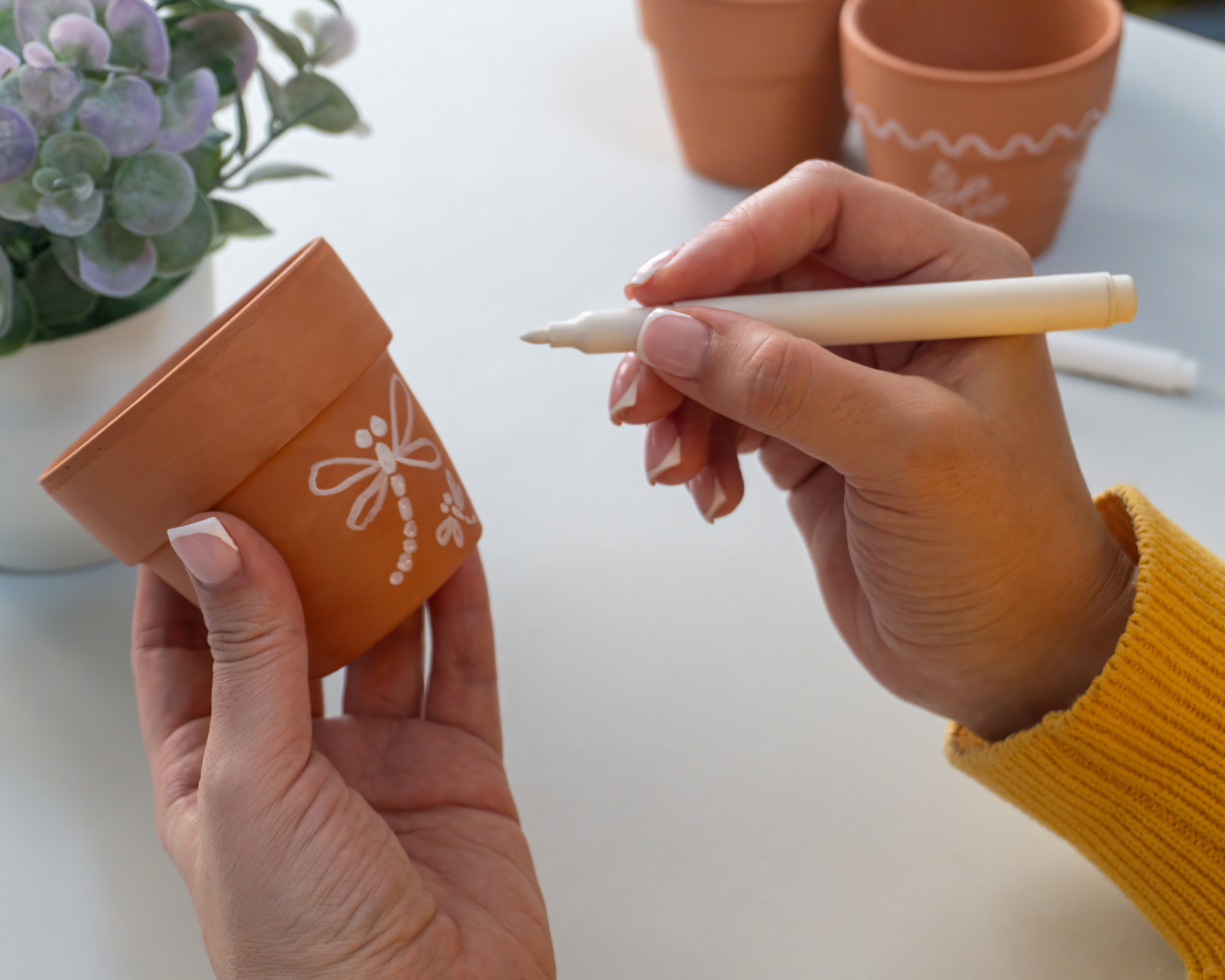 person using acrylic paint markers to draw on and decorate terracotta pots