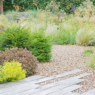 An outdoor space with assortment of gravel, shubbery and decorative decking arrangement