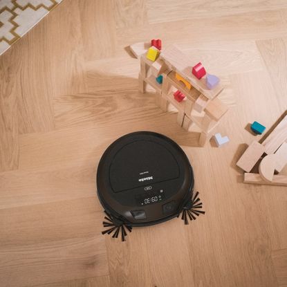 Miele Scout RX3 Home Vision HD on a wooden floor next to children's wooden building blocks