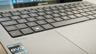 A silver ASUS Zenbook S 13 OLED laptop sitting on a wooden desk