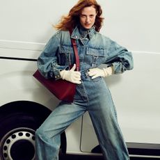 Young woman wearing blue denim overalls from The Outnet, stood in front of white van.