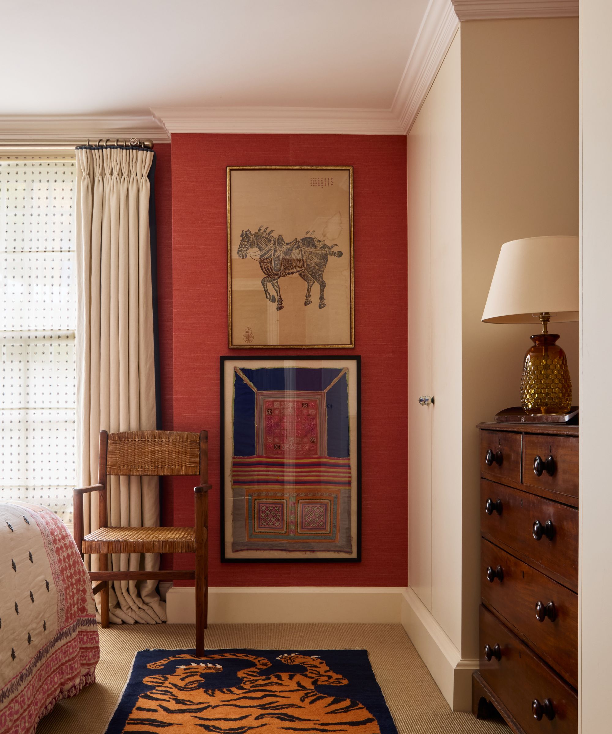 Bedroom with red grasscloth wall, jute carpet, tiger rug, antique chair and dresser