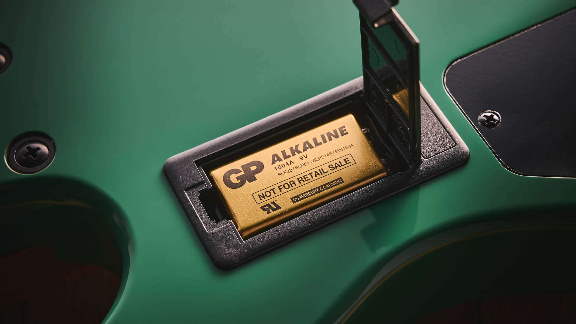 The Cort GB-Short Scale Bass finished in green, photographed against a light wooden floor and rug.