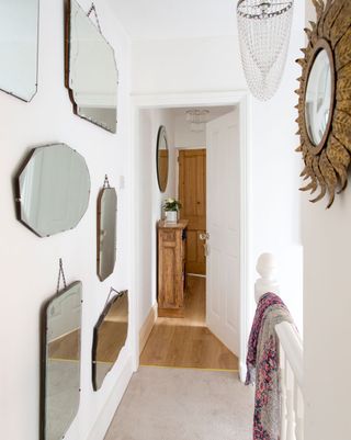 Feature wall of mirrors on a white wall leading to the wooden front door