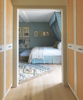 blue and white bedroom seen through a walk in closet with rattan panelled wardrobe doors and a blue and white bedroom with a canopy bed