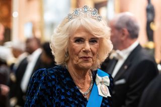 Queen Camilla wears a blue velvet gown with Queen Elizabeth's aquamarine ribbon tiara and matching earrings and a necklace