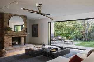 A modern minimalist living room with a large brick fireplace, floor to ceiling windows, and a dark marble coffee table