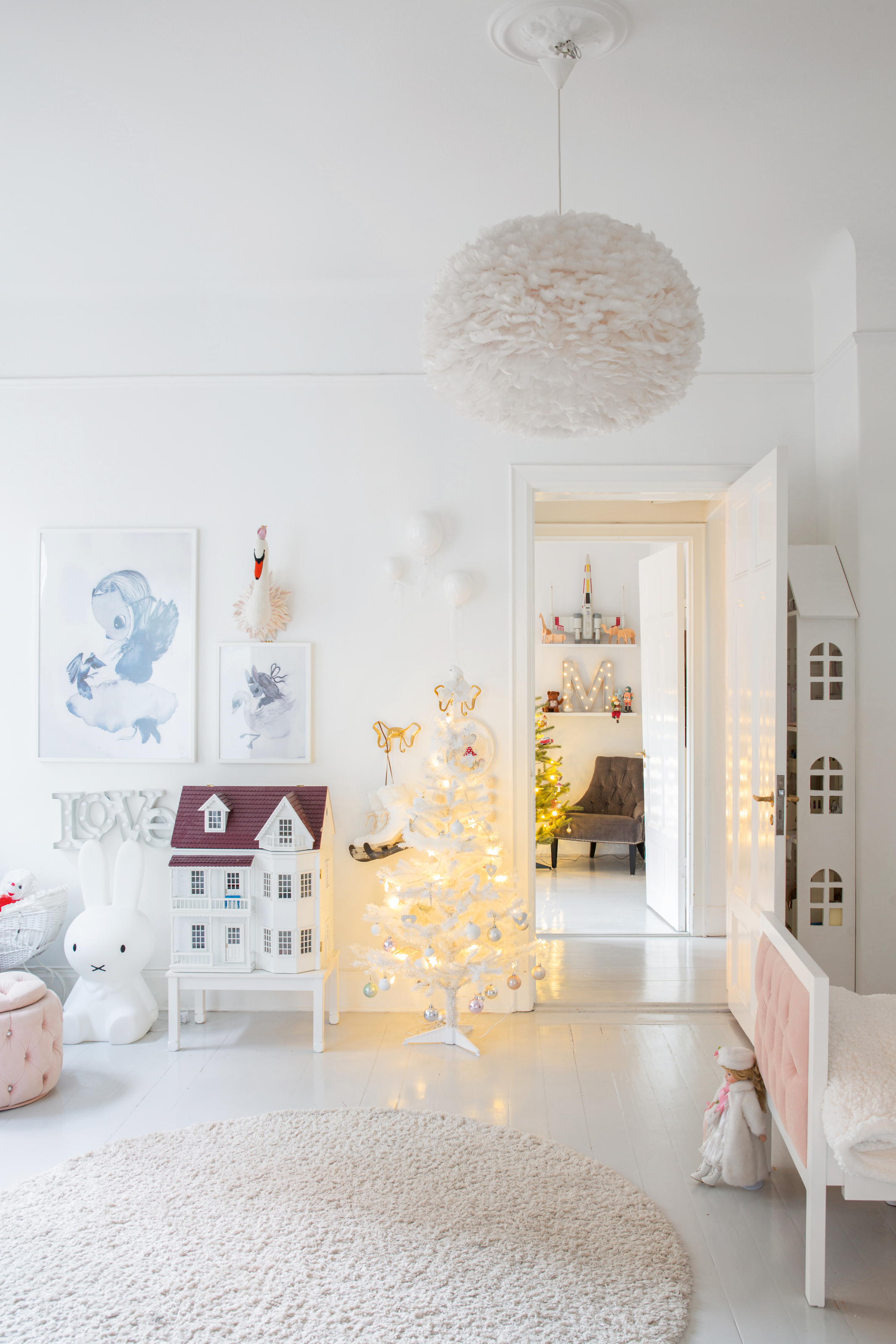 White kid&#039;s room with white doll house, small white lit-up tree and white fluffy ceiling light