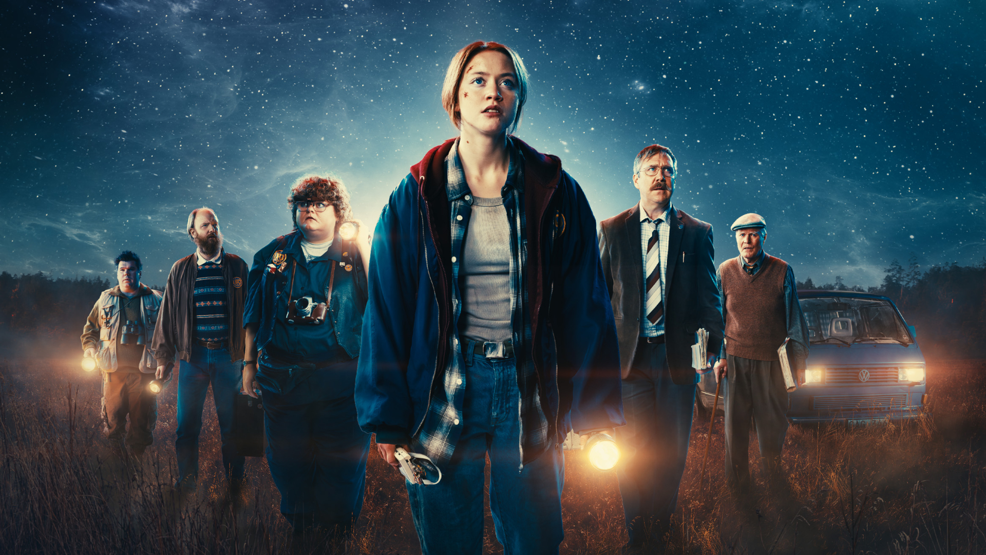a group of six people assembled at night before a cosmic backdrop