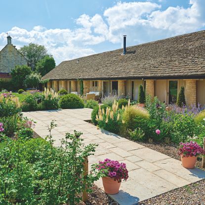 exterior of single storey converted cowshed with paving surrounded by country cottage flowers