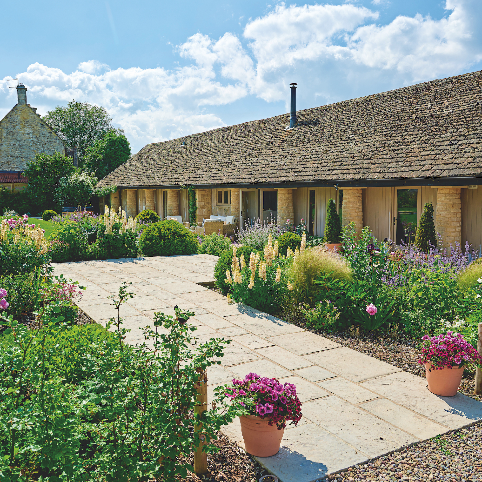 exterior of single storey converted cowshed with paving surrounded by country cottage flowers