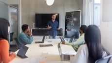Business strategy meeting showing a man presenting to colleagues in an open plan office space.