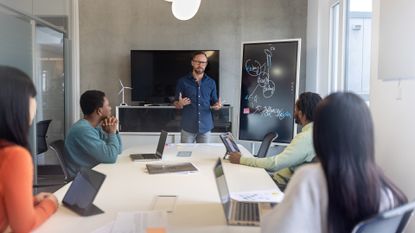 Business strategy meeting showing a man presenting to colleagues in an open plan office space.