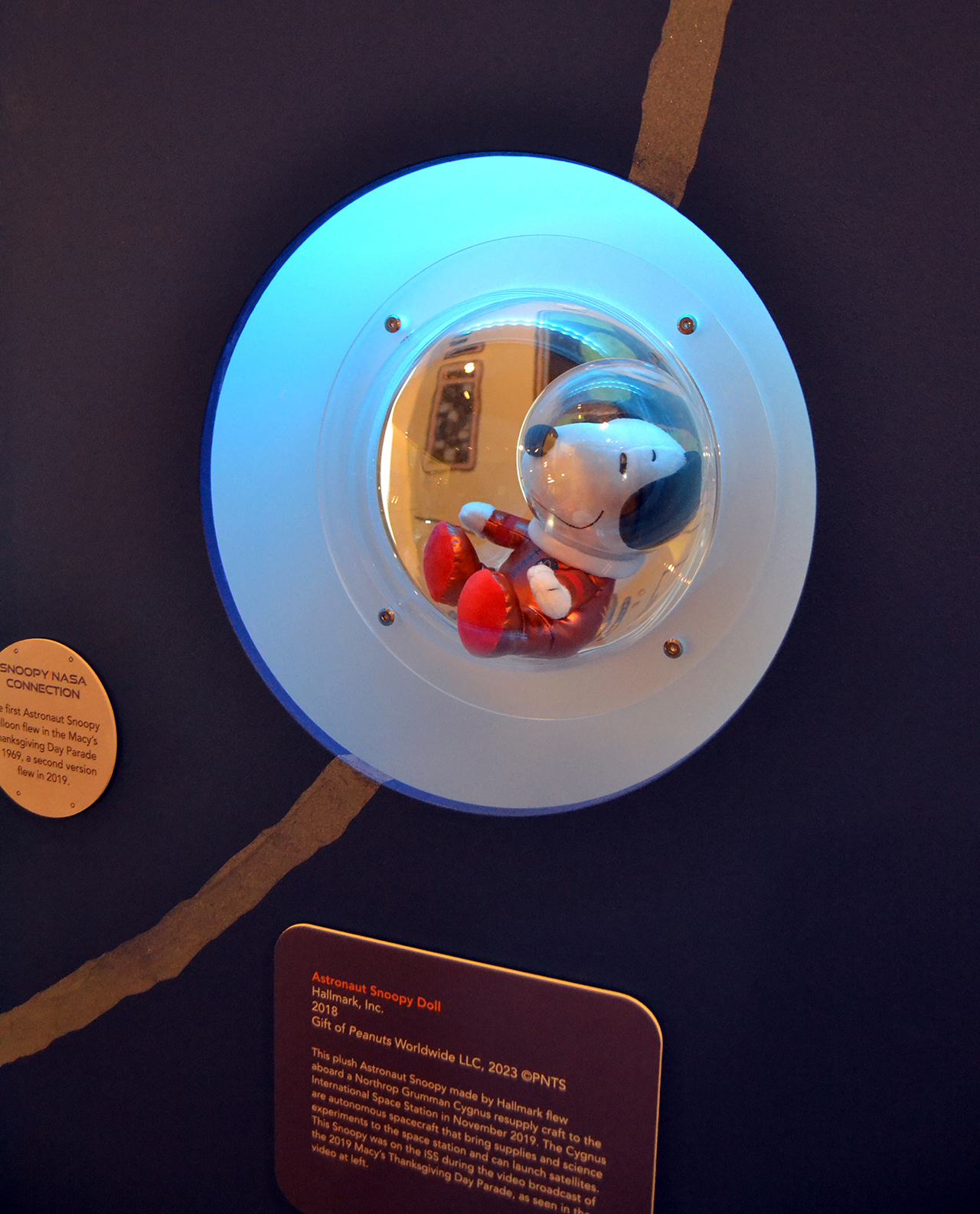 a plush astronaut Snoopy doll wearing a spacesuit on display at a museum